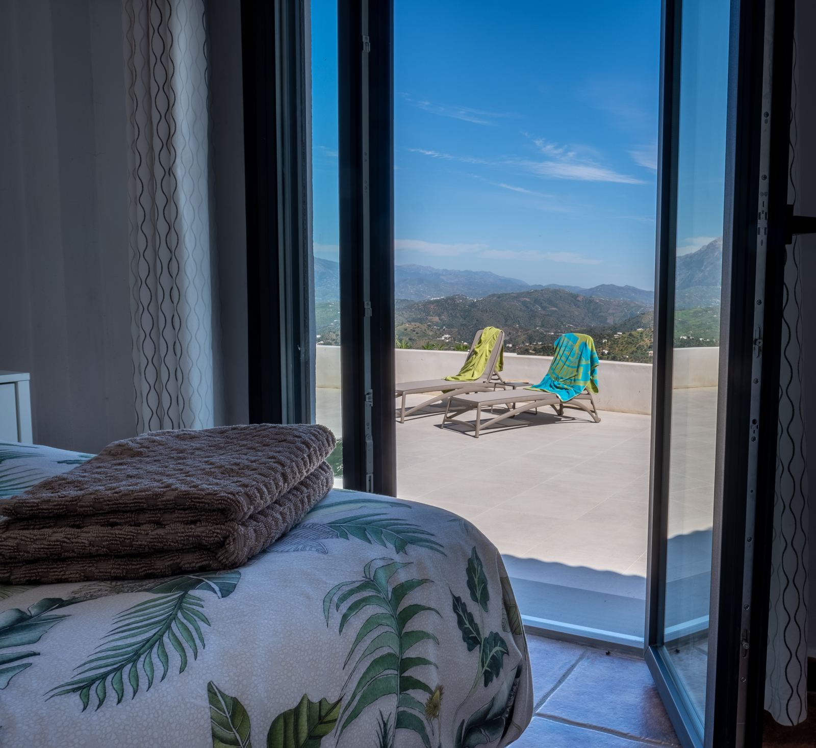 Master bedroom met openslaande deuren en directe toegang tot het terras met ligstoelen en bergzicht